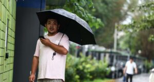 China declara alertas rojas por lluvias e inundaciones Hombre en China sosteniendo un paraguas negro bajo la lluvia mientras mira su teléfono móvil.