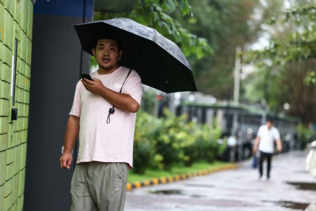 Alertas máximas por fuertes lluvias en varios puntos del centro y el sur de China Hombre en China sosteniendo un paraguas negro bajo la lluvia mientras mira su teléfono móvil.