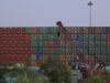 EE. UU. impone aranceles del 100% a los drones de China Muro de contenedores de carga apilados en un puerto comercial con una grúa roja en primer plano.