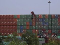 EE. UU. impone aranceles del 100% a los drones de China Muro de contenedores de carga apilados en un puerto comercial con una grúa roja en primer plano.