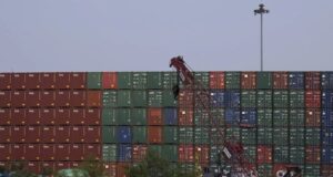 EE. UU. impone aranceles del 100% a los drones de China Muro de contenedores de carga apilados en un puerto comercial con una grúa roja en primer plano.