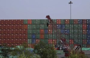 EE. UU. impone aranceles del 100% a los drones de China Muro de contenedores de carga apilados en un puerto comercial con una grúa roja en primer plano.