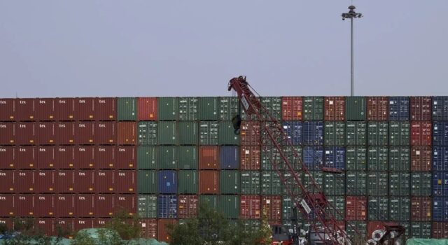 EE. UU. impone aranceles del 100% a los drones de China Muro de contenedores de carga apilados en un puerto comercial con una grúa roja en primer plano.