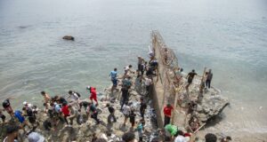 Marruecos culpa a fallo judicial español por crisis en Ceuta Decenas de personas agrupadas sobre rocas intentando rodear el espigón fronterizo con valla metálica hacia Ceuta.