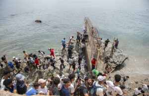 Marruecos culpa a fallo judicial español por crisis en Ceuta Decenas de personas agrupadas sobre rocas intentando rodear el espigón fronterizo con valla metálica hacia Ceuta.