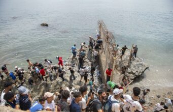 Marruecos culpa a fallo judicial español por crisis en Ceuta Decenas de personas agrupadas sobre rocas intentando rodear el espigón fronterizo con valla metálica hacia Ceuta.