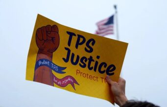 Deportados de EE. UU. llegan a Haití tras la cancelación del TPS Cartel de protesta por el fin del TPS para deportados de Haití frente a bandera de Estados Unidos.