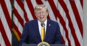 EE. UU. planea cobrar una nueva tarifa de 100.000 dólares para visas H-1B Donald Trump sonriendo en un podio presidencial ante banderas de EE. UU. respecto a las tarifas de visas H-1B.