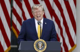 EE. UU. planea cobrar una nueva tarifa de 100.000 dólares para visas H-1B Donald Trump sonriendo en un podio presidencial ante banderas de EE. UU. respecto a las tarifas de visas H-1B.