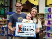 Homewood Public Library lanza iniciativas por tarjeta de biblioteca Familia con un bebé sostiene un cartel de las bibliotecas del condado de Jefferson en Alabama.