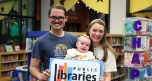 Homewood Public Library lanza iniciativas por tarjeta de biblioteca Familia con un bebé sostiene un cartel de las bibliotecas del condado de Jefferson en Alabama.