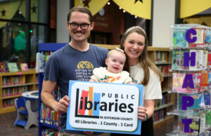 Homewood Public Library lanza iniciativas por tarjeta de biblioteca Familia con un bebé sostiene un cartel de las bibliotecas del condado de Jefferson en Alabama.