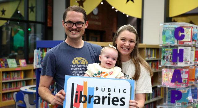 Homewood Public Library lanza iniciativas por tarjeta de biblioteca Familia con un bebé sostiene un cartel de las bibliotecas del condado de Jefferson en Alabama.