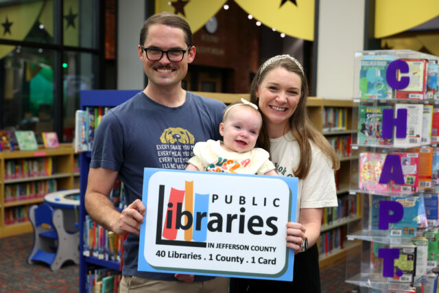 Familia con un bebé sostiene un cartel de las bibliotecas del condado de Jefferson en Alabama.
