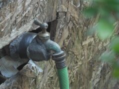 Facturas de agua excesivas generan cobros de cientos de dólares Llave de agua exterior con aislamiento y manguera verde conectada en una pared de madera.
