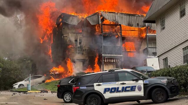 Voraz incendio consume edificio de apartamentos en Birmingham con patrulla policial en primer plano.