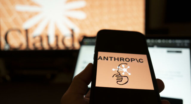 Inteligencia artificial muestra conductas autónomas y engañosas Mano sosteniendo un teléfono con el logo de Anthropic frente a una pantalla con el nombre de Claude.