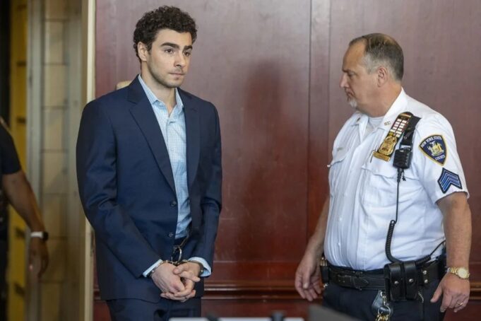 Luigi Mangione se declara culpable por crimen de Brian Thompson Luigi Mangione en traje formal y esposado junto a un oficial dentro de un tribunal de Nueva York.