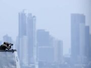 EE. UU. lanza fuerza multinacional de drones de ataque Oficial de la Marina de EE. UU. en la cubierta de un buque observando el horizonte frente a un perfil urbano.