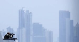 EE. UU. lanza fuerza multinacional de drones de ataque Oficial de la Marina de EE. UU. en la cubierta de un buque observando el horizonte frente a un perfil urbano.