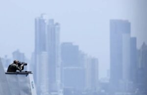 EE. UU. lanza fuerza multinacional de drones de ataque Oficial de la Marina de EE. UU. en la cubierta de un buque observando el horizonte frente a un perfil urbano.