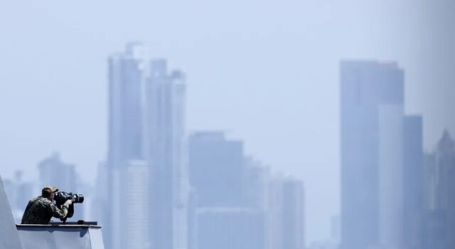 EE. UU. lanza fuerza multinacional de drones de ataque Oficial de la Marina de EE. UU. en la cubierta de un buque observando el horizonte frente a un perfil urbano.