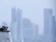 EE. UU. lanza fuerza multinacional de drones de ataque Oficial de la Marina de EE. UU. en la cubierta de un buque observando el horizonte frente a un perfil urbano.