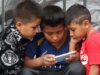 Prohibición de celulares en escuelas de México abre debate Tres niños observan la pantalla de un celular en México durante la regulación de dispositivos escolares.