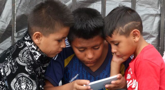 Prohibición de celulares en escuelas de México abre debate Tres niños observan la pantalla de un celular en México durante la regulación de dispositivos escolares.