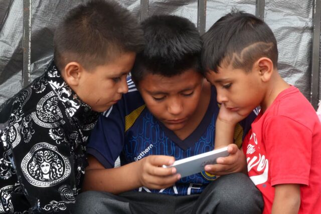 Prohibición de celulares en escuelas de México abre debate Tres niños observan la pantalla de un celular en México durante la regulación de dispositivos escolares.