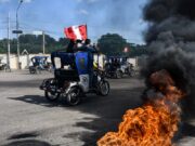 Subsidio a combustibles en Perú aliviará a transportistas Mototaxis con banderas de Perú protestan en una calle bloqueada con neumáticos en llamas.