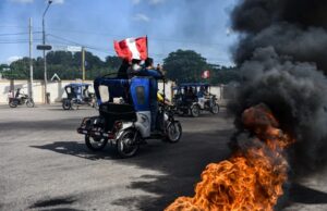 Subsidio a combustibles en Perú aliviará a transportistas Mototaxis con banderas de Perú protestan en una calle bloqueada con neumáticos en llamas.