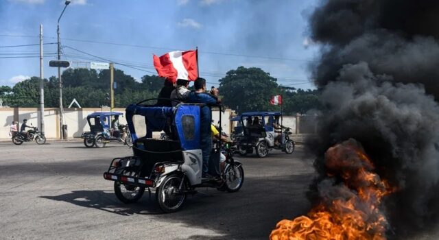 Subsidio a combustibles en Perú aliviará a transportistas Mototaxis con banderas de Perú protestan en una calle bloqueada con neumáticos en llamas.
