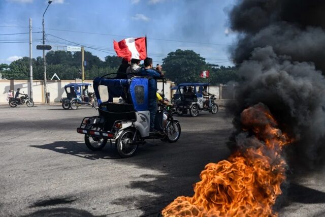 protestas-mototaxis-combustible-ucayali-peru Mototaxis con banderas de Perú protestan en una calle bloqueada con neumáticos en llamas.