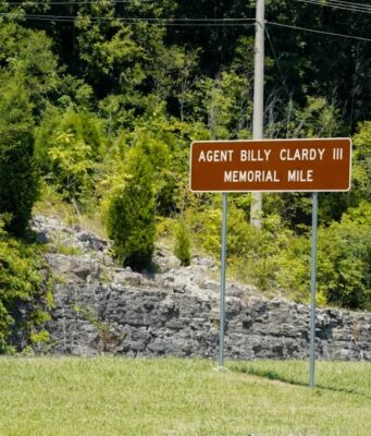 Dedican tramo de la U.S. 72 al agente Billy Clardy III Señal de tránsito marrón con la inscripción Agent Billy Clardy III Memorial Mile a la orilla de la carretera.