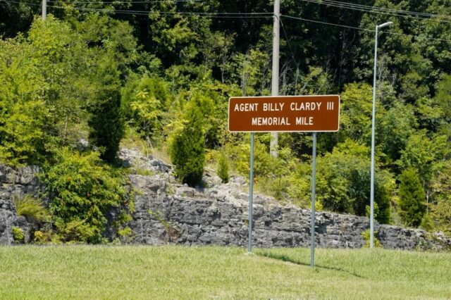Señal de tránsito marrón con la inscripción Agent Billy Clardy III Memorial Mile a la orilla de la carretera.