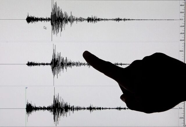 Silueta de un dedo señalando un sismograma con ondas sísmicas de un terremoto en Indonesia.