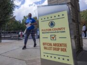 Justicia de EE. UU. respalda restricciones al voto por correo Buzón de entrega de voto por correo de Fulton County en Estados Unidos con una votante caminando al fondo.