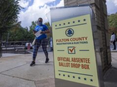 Justicia de EE. UU. respalda restricciones al voto por correo Buzón de entrega de voto por correo de Fulton County en Estados Unidos con una votante caminando al fondo.