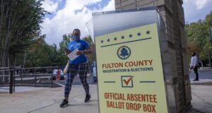 Justicia de EE. UU. respalda restricciones al voto por correo Buzón de entrega de voto por correo de Fulton County en Estados Unidos con una votante caminando al fondo.