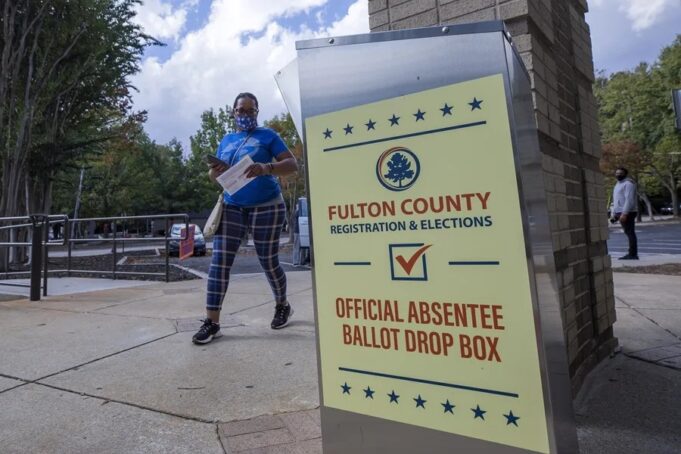 Justicia de EE. UU. respalda restricciones al voto por correo Buzón de entrega de voto por correo de Fulton County en Estados Unidos con una votante caminando al fondo.