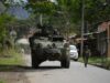 Órdenes de captura contra 46 exnegociadores en Colombia Vehículo blindado militar y soldado patrullando una calle rural en Colombia tras reactivación de capturas.