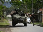 Órdenes de captura contra 46 exnegociadores en Colombia Vehículo blindado militar y soldado patrullando una calle rural en Colombia tras reactivación de capturas.