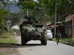 Órdenes de captura contra 46 exnegociadores en Colombia Vehículo blindado militar y soldado patrullando una calle rural en Colombia tras reactivación de capturas.