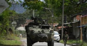 Órdenes de captura contra 46 exnegociadores en Colombia Vehículo blindado militar y soldado patrullando una calle rural en Colombia tras reactivación de capturas.
