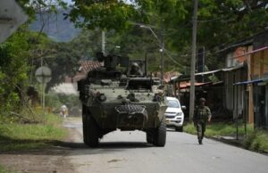 Órdenes de captura contra 46 exnegociadores en Colombia Vehículo blindado militar y soldado patrullando una calle rural en Colombia tras reactivación de capturas.