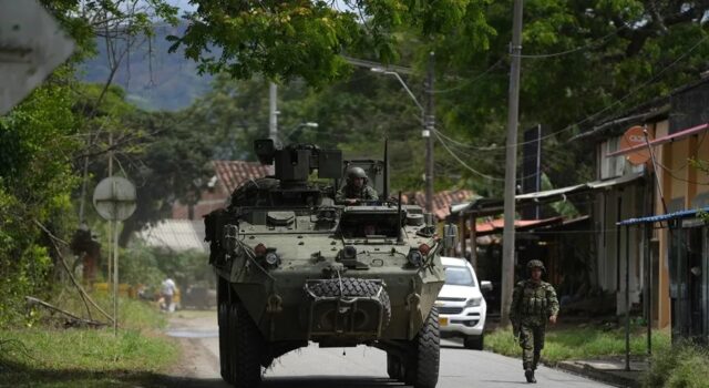 Órdenes de captura contra 46 exnegociadores en Colombia Vehículo blindado militar y soldado patrullando una calle rural en Colombia tras reactivación de capturas.