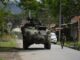 Órdenes de captura contra 46 exnegociadores en Colombia Vehículo blindado militar y soldado patrullando una calle rural en Colombia tras reactivación de capturas.