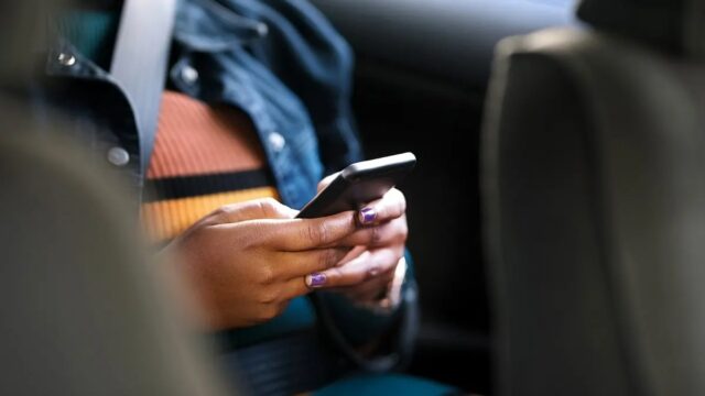 pasajera-usando-telefono-movil-en-auto-motion-assist Pasajera con cinturón de seguridad usando un smartphone en un coche para probar Motion Assist contra el mareo.